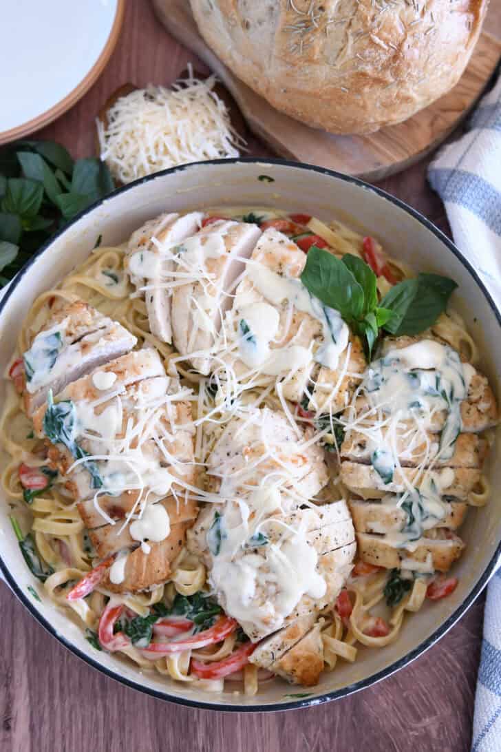 Top down view of sauteed chicken breasts on top of pasta, Parmesan cream sauce, spinach and peppers.