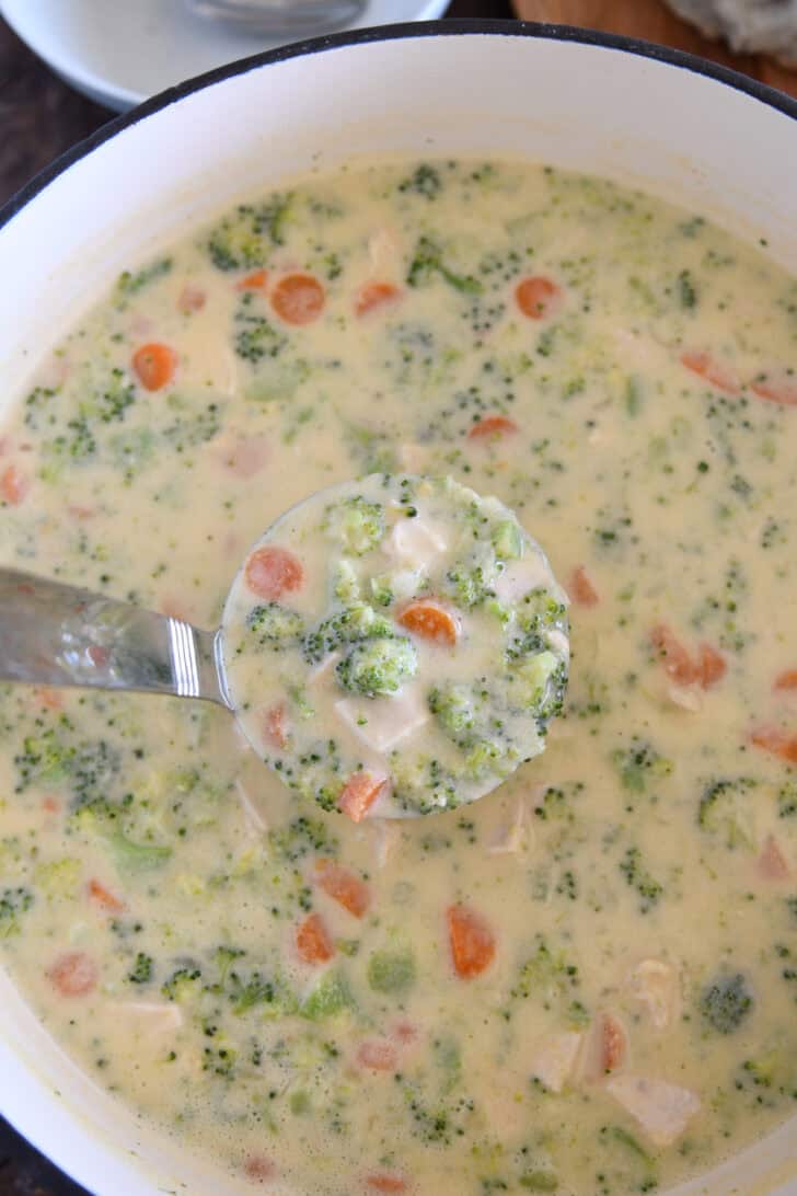 Ladle scooping up ladleful of cheesy chicken broccoli soup with carrots.