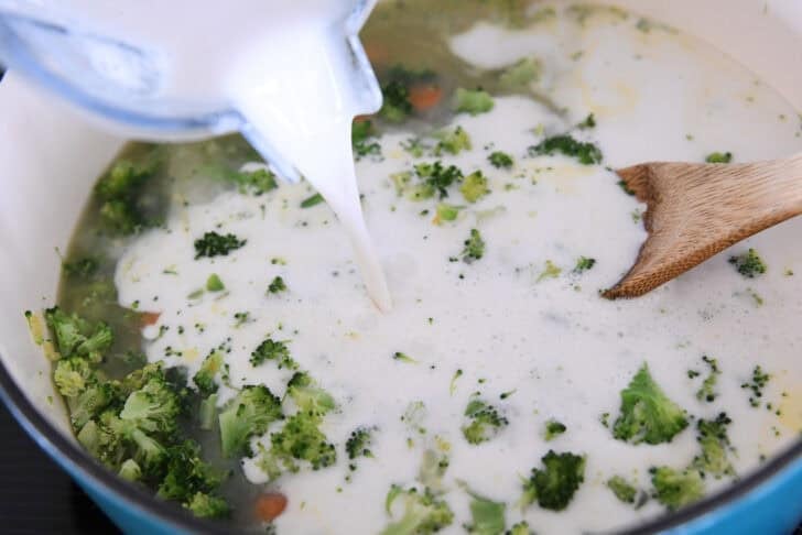 Adding cream and cornstarch to soup pot with broccoli and carrots.
