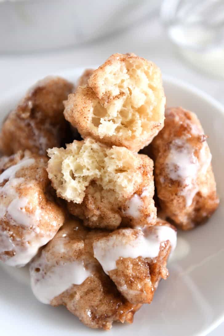 White plate with five cinnamon roll bites drizzled with icing with top cinnamon roll bite in half.