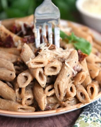 Brown rimmed plate with cooked Instant Pot marry. me pasta with sun-dried tomatoes on top with fresh basil.