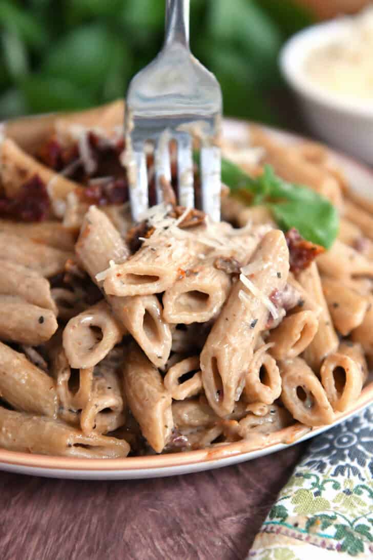Brown rimmed plate with cooked Instant Pot marry. me pasta with sun-dried tomatoes on top with fresh basil.