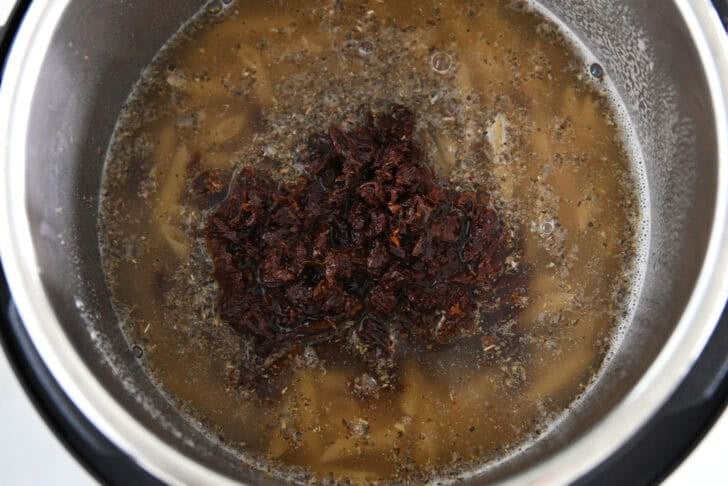 Instant pot with sun-dried tomatoes, broth, seasonings and pasta.