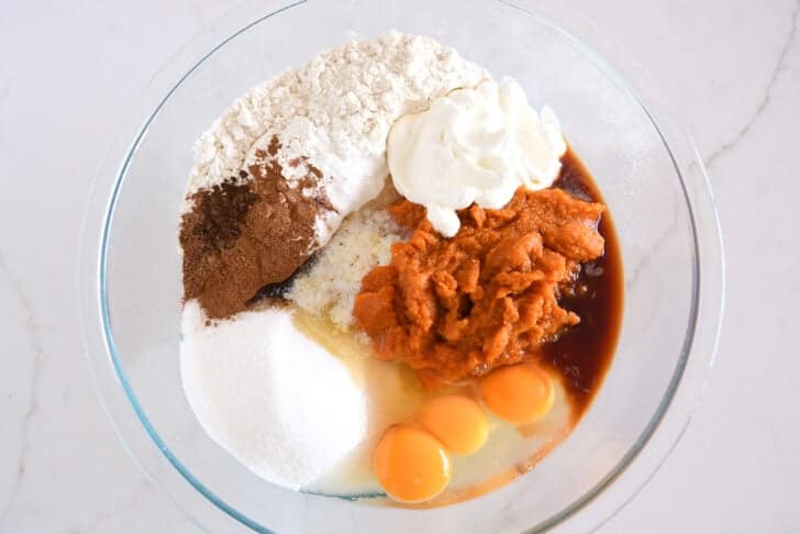 Glass bowl with eggs, canned pumpkin, sour cream, flour, granulated sugar, vanilla, cinnamon and salt.