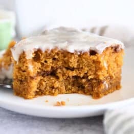 One square of pumpkin cinnamon swirl cake on white plate with bite taken out.
