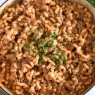Top down view of cooked pasta, sauce, seasonings, ground beef in white cast iron skillet and topped with chopped parsley.