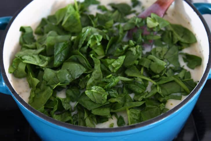 Fresh spinach added to cast iron enamel pot with gnocchi soup.