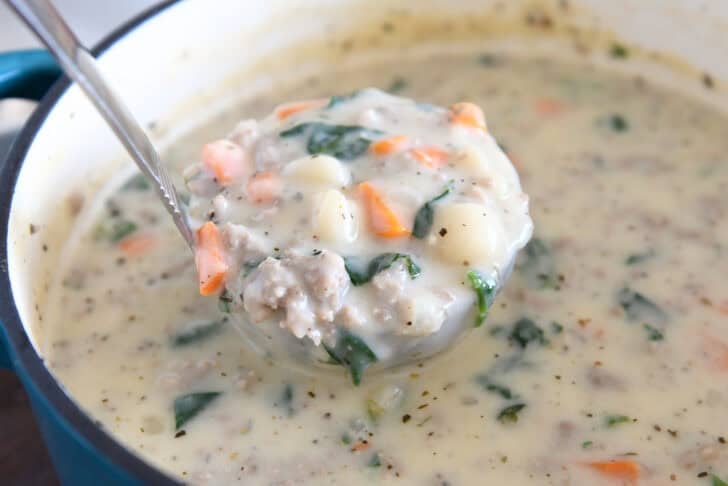 Ladle scooping up creamy soup with gnocchi, sausage, spinach, and carrots.