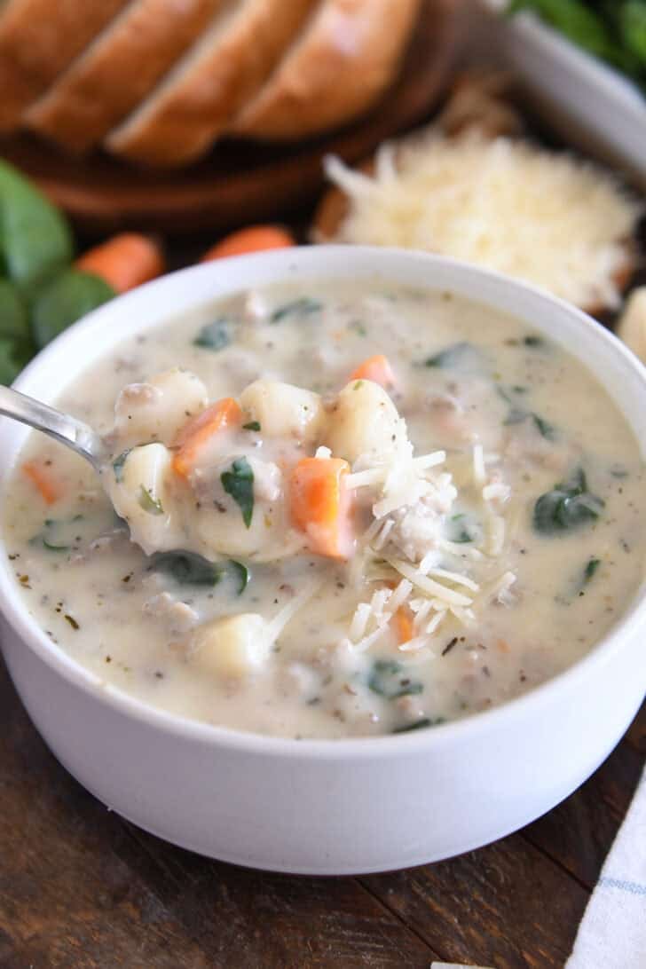 White soup bowl with spoon scooping up creamy soup with carrots, gnocchi, spinach, sausage and freshly grated Parmesan cheese.