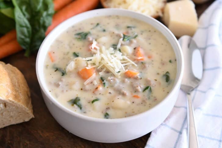 Top down view of creamy soup with carrots, gnocchi, spinach, sausage and freshly grated Parmesan cheese.
