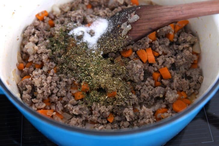 Cast iron enamel pot with cooked sausage, carrots, dried basil, dried oregano and salt.