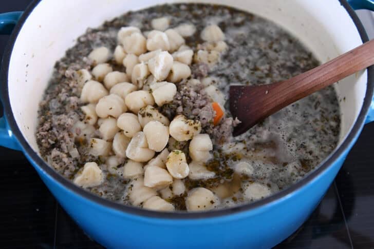 Cast iron pot with cooked sausage, broth, and gnocchi.