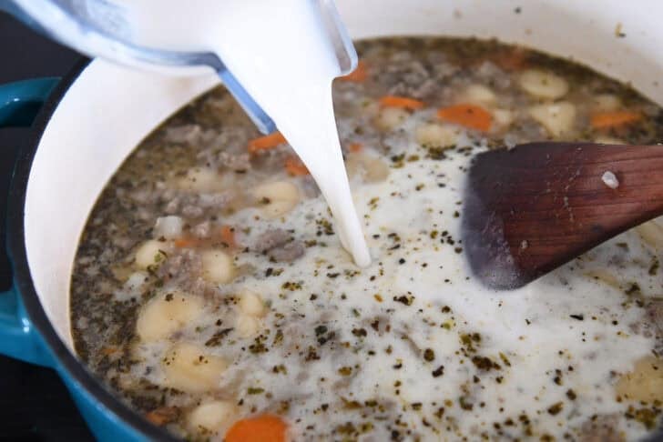 Pouring flour and milk mixture into pot with broth, gnocchi, cooked sausage and carrots.