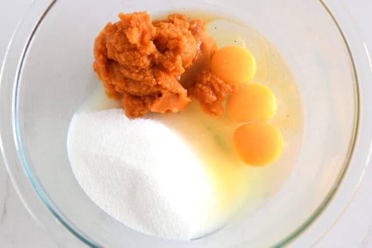 Glass bowl with granulated sugar, canned pumpkin and eggs.