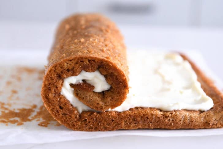 Pumpkin sheet cake starting to be rolled up with cream cheese frosting.