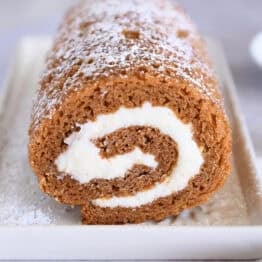 Pumpkin roll on white tray sprinkled with powdered sugar.