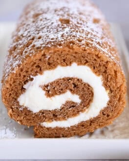 Pumpkin roll on white tray sprinkled with powdered sugar.