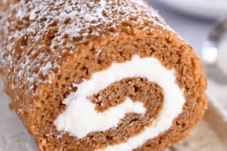 Pumpkin roll on white tray sprinkled with powdered sugar.