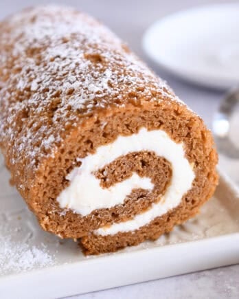 Pumpkin roll on white tray sprinkled with powdered sugar.
