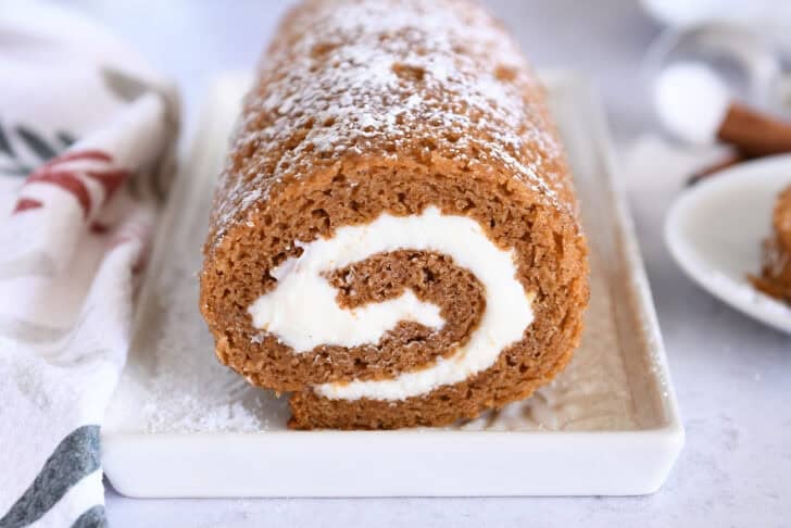 Pumpkin roll on white tray sprinkled with powdered sugar.