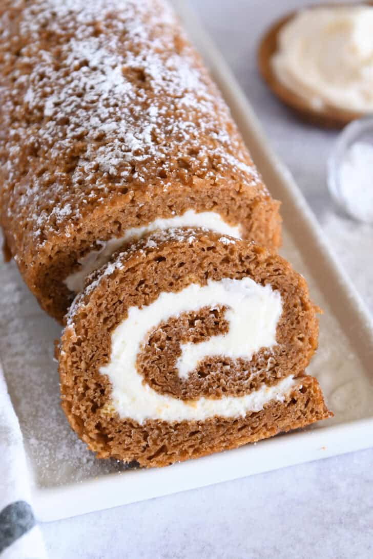 Pumpkin roll on white tray with one slice cut.