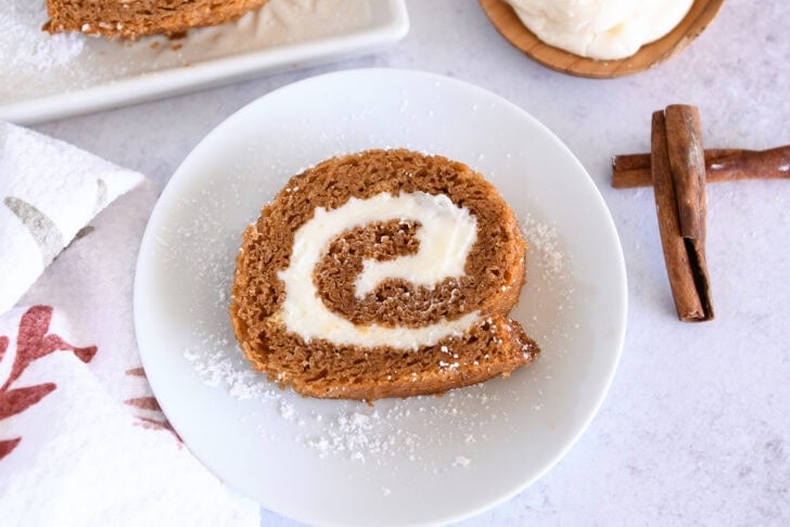 Slice of pumpkin roll on white plate.