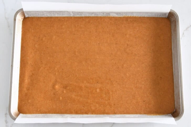 Sheet pan with parchment and pumpkin cake batter.
