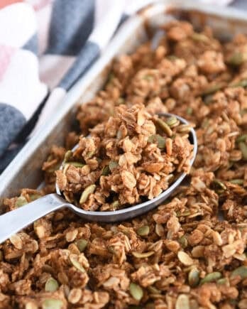 Sheet pan with baked pumpkin pecan granola with deep metal spoon scooping up granola.