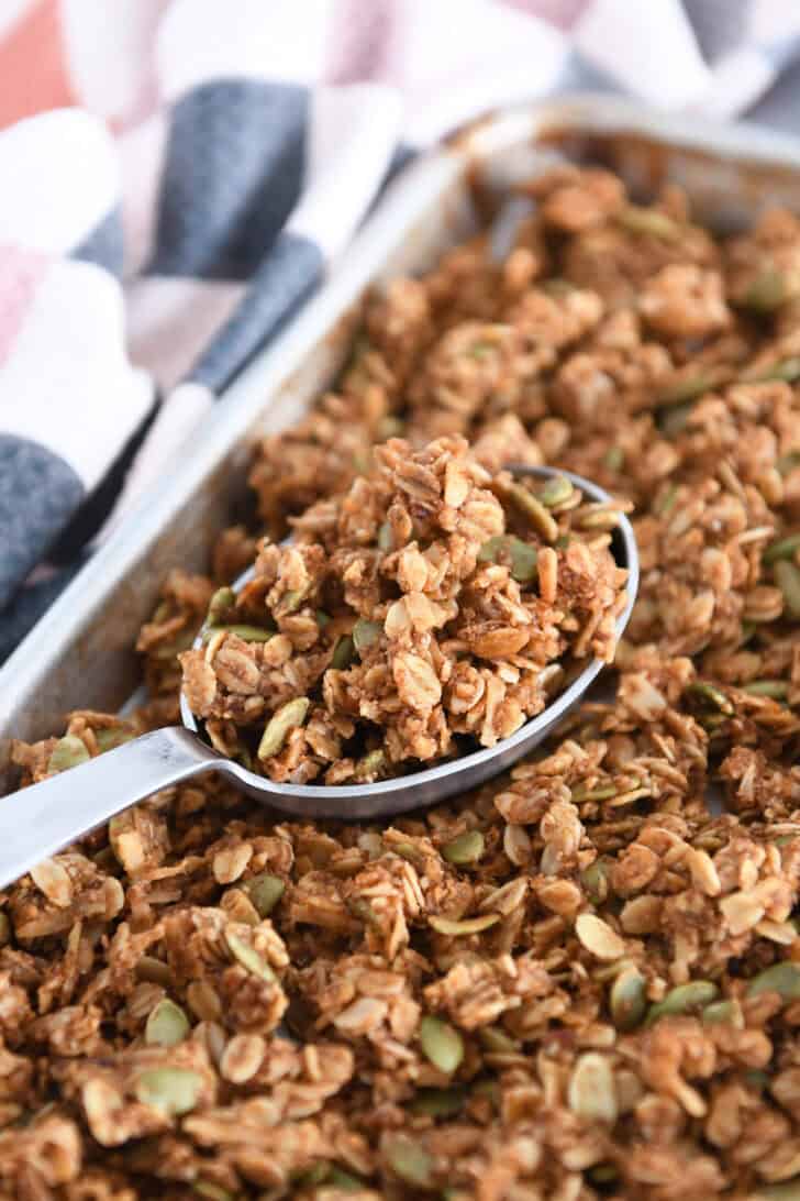 Sheet pan with baked pumpkin pecan granola with deep metal spoon scooping up granola.
