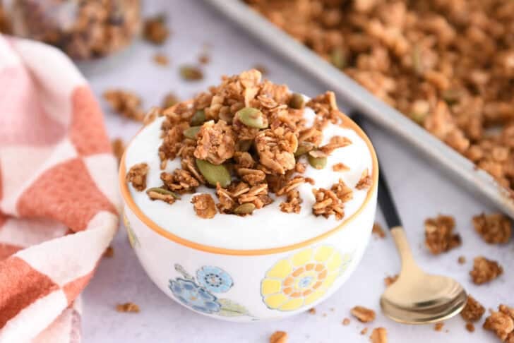 White bowl with orange rim filled with vanilla yogurt and topped with brown butter pumpkin pecan granola with roasted pumpkin seeds.