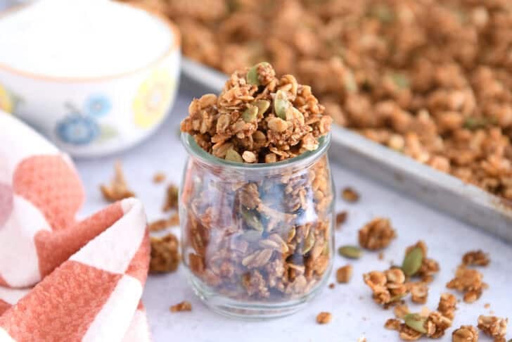 Small glass jar filled with brown butter pumpkin pecan granola with roasted pumpkin seeds.