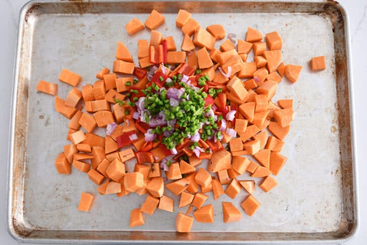 Sheet pan with raw diced sweet potatoes, jalapenos, onions, and red peppers.