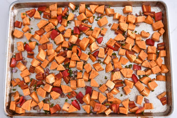 Sweet potatoes, red peppers, onions and jalapenos scattered across sheet pan.