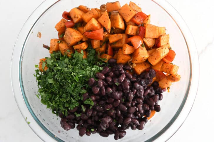 Glass bowl with roasted sweet potatoes, red pepeprs, cilantro and black beans.