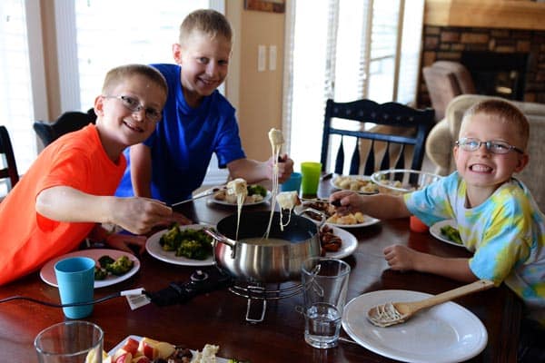 Three smiling boys surrounding a fondue pot dipping their food in.