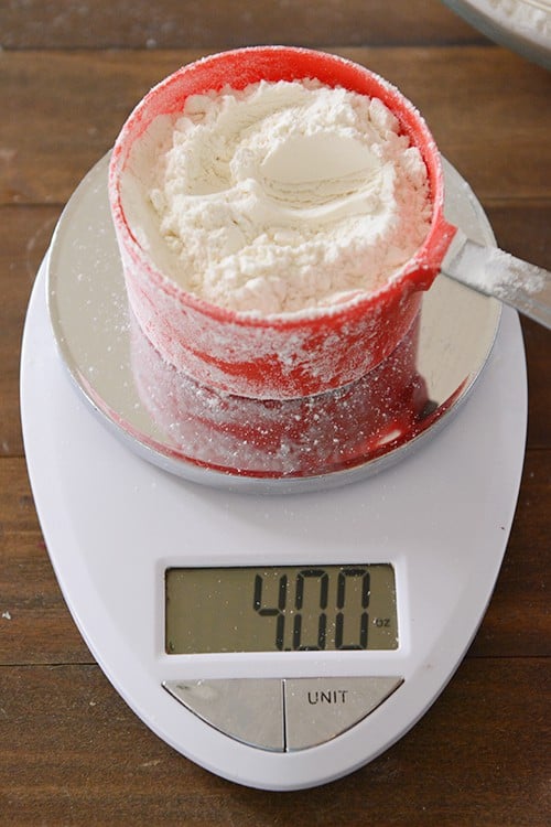 A digital kitchen scale measuring a partially filled measuring cup of flour. 