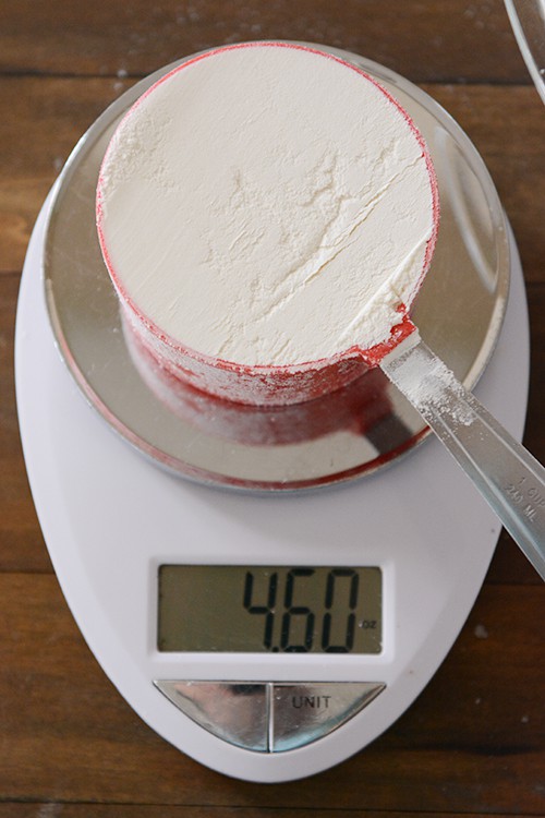 A red measuring cup full of flour on a kitchen scale. 