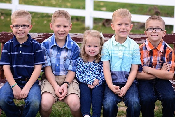 Five little kids sitting next to each other on an old wood bench.