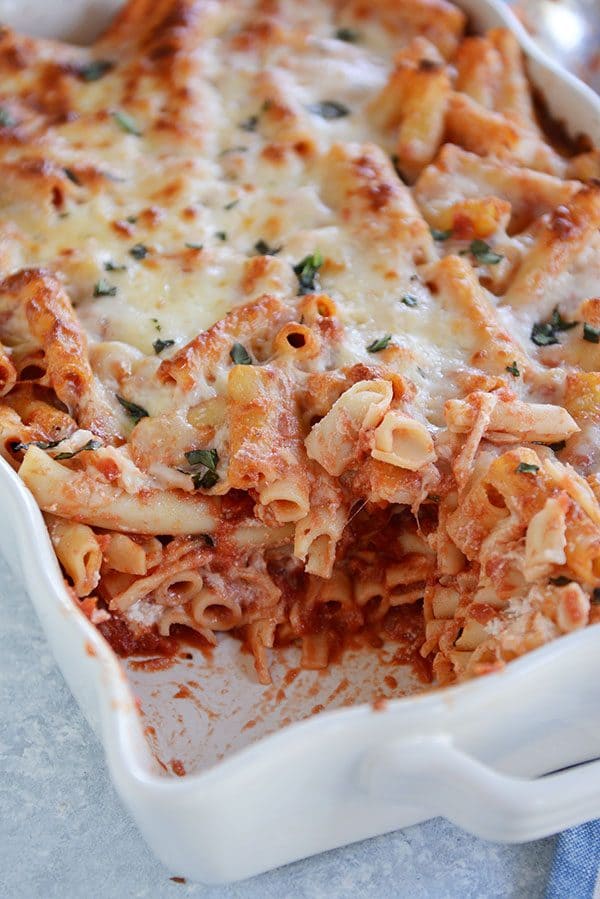 A casserole dish of cheesy baked ziti with a scoop taken out of the corner.