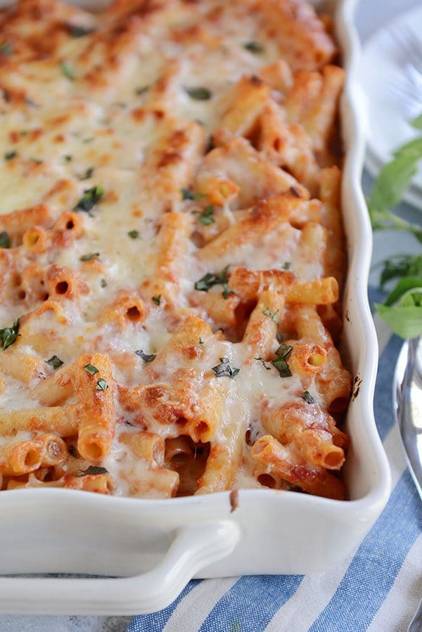 A white casserole dish full of cheese-topped baked ziti sprinkled with cilantro.