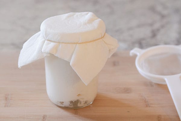 A paper towel covered mason jar full of kefir milk.