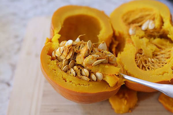 A large metal spoon scooping the insides of a pumpkin out.