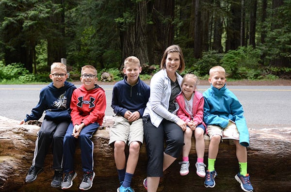 A Mom sitting on a log with her five kids.