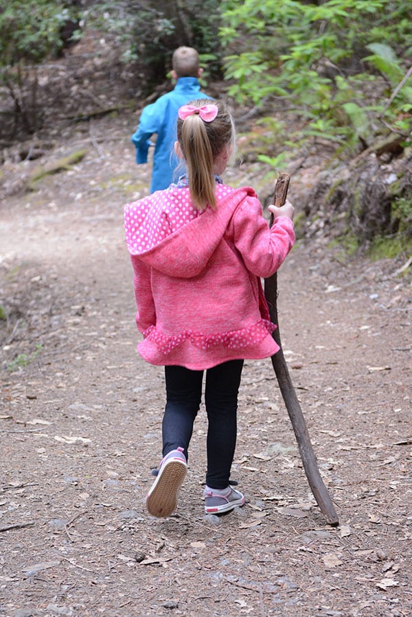 A little girl hiking with a walking stick.