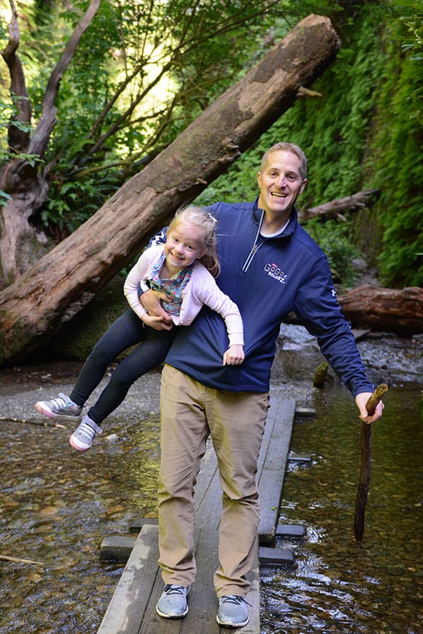 A Dad holding his daughter and crossing a wooden bridge.