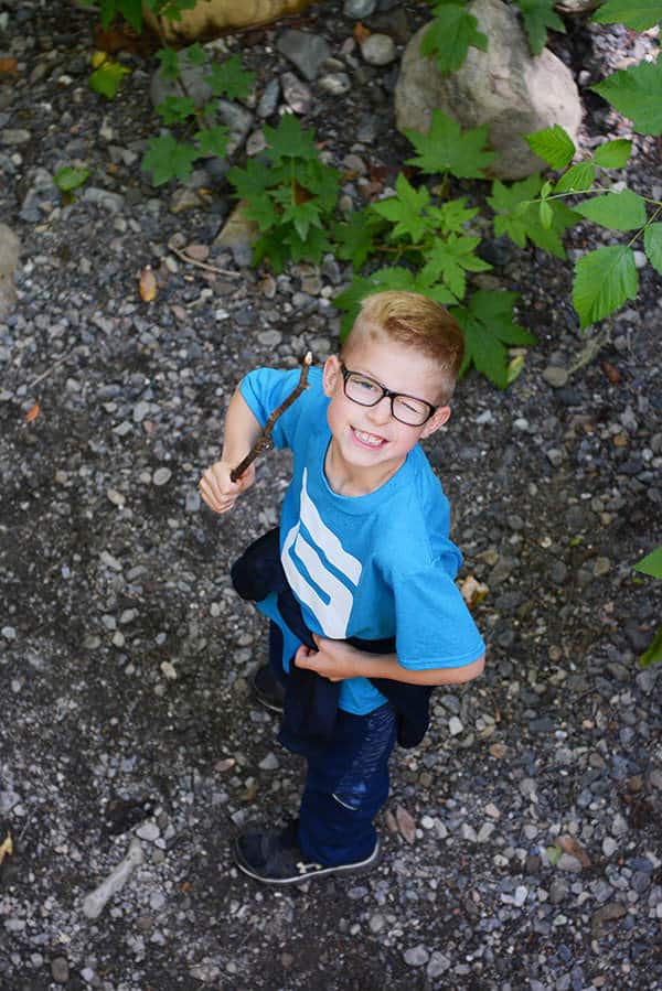 A little boy with glasses holding a stick and winking at the camera.