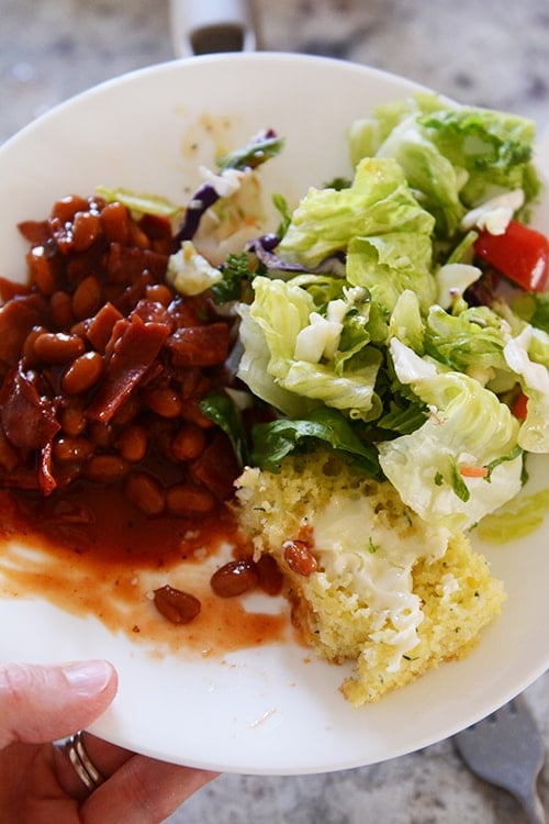 A white plate of cornbread, baked beans, and green salad.