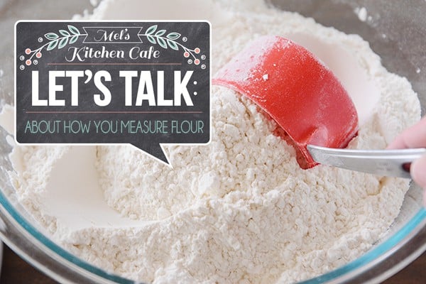 A red measuring cup scooping flour out of a clear glass bowl.