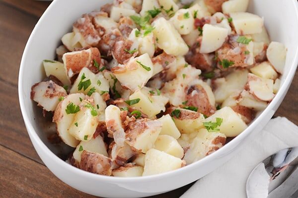 An oval bowl full of german potato salad topped with chopped parsley.