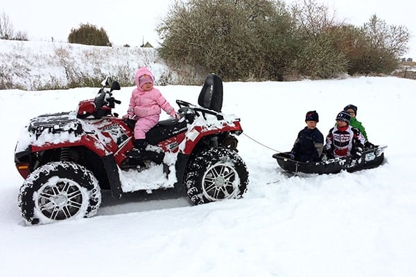 Little kids sledding behind a 4-wheeler.